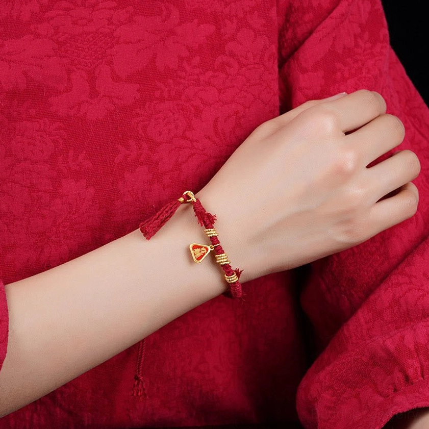 Woman wearing red string goddess protection bracelet on wrist, showing side angle view with small gold ornaments against red clothing