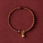 Red gold braided lotus bracelet with dark red bead and gold lotus charm pendant - flat lay view