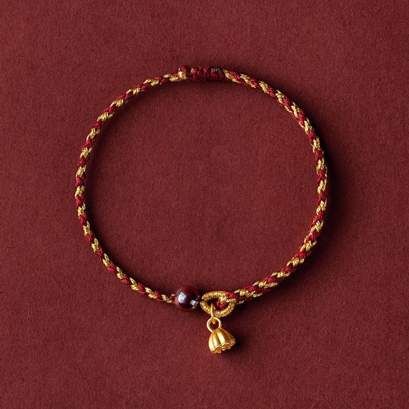 Red gold braided lotus bracelet with dark red bead and gold lotus charm pendant - flat lay view