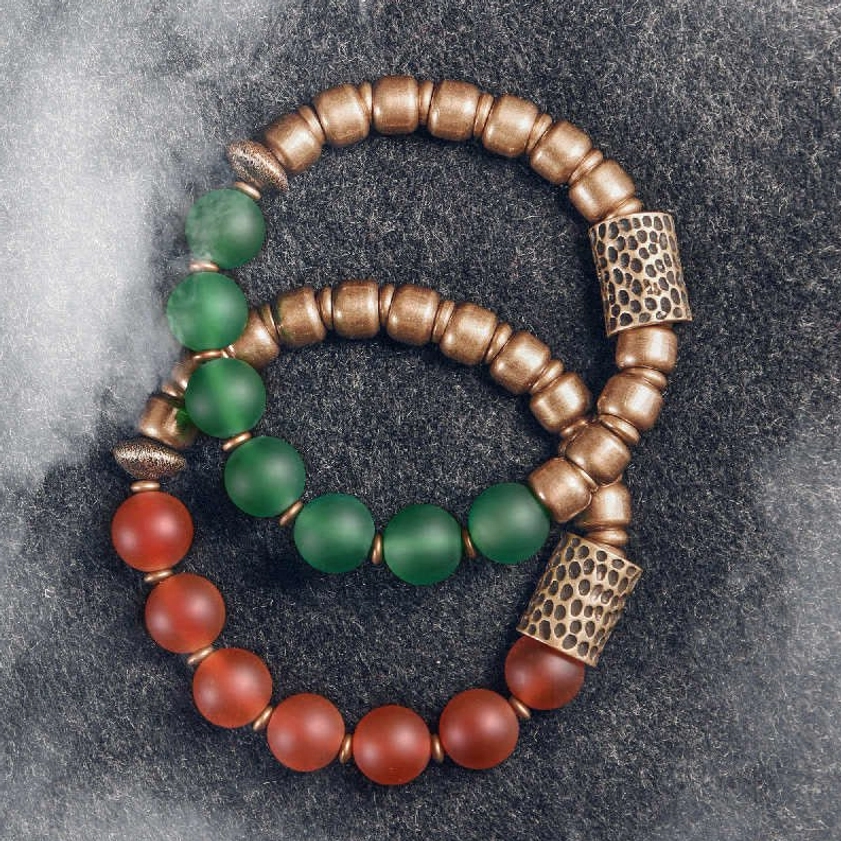 Red and green agate Buddhist bracelets set with copper accents displayed together on dark background
