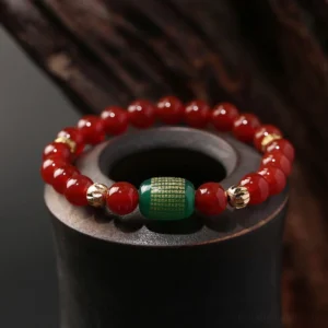 Red and green agate Buddhist sutra bracelet with gold-plated copper spacers displayed on dark wooden stand, close-up overhead view