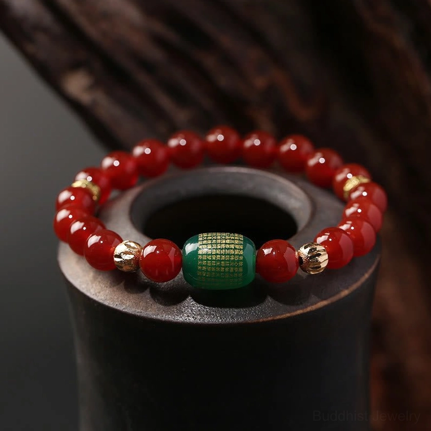 Red and green agate Buddhist sutra bracelet with gold-plated copper spacers displayed on dark wooden stand, close-up overhead view