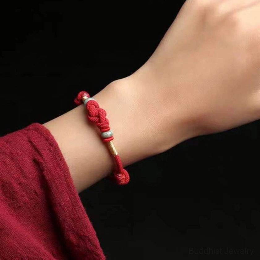 Red string jade bracelet worn on clothed wrist with red fabric sleeve showing compact woven bracelet design in lifestyle setting