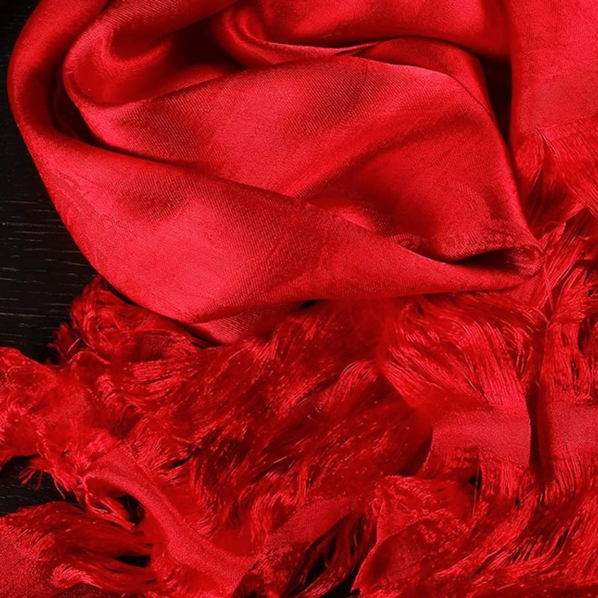 Bright red five-color Buddhist khata scarf with thick frayed silk-like tassels and glossy texture on dark wooden background