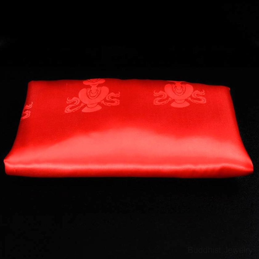 Single red blessing khata scarf flat overhead view on black background with bright red satin and embossed red religious patterns