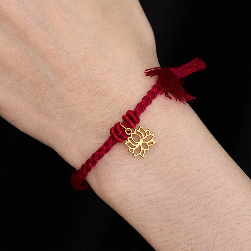 Red lotus Buddhist bracelet worn on wrist against black background showing how gold lotus pendant sits when worn