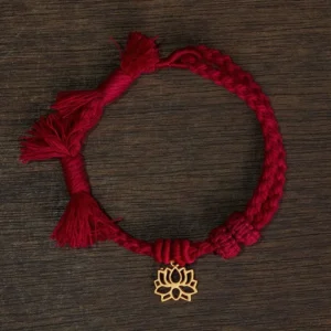 Red Buddhist lotus string bracelet flat lay showing burgundy braided cord with gold hollow lotus pendant and tasseled ends on wooden surface