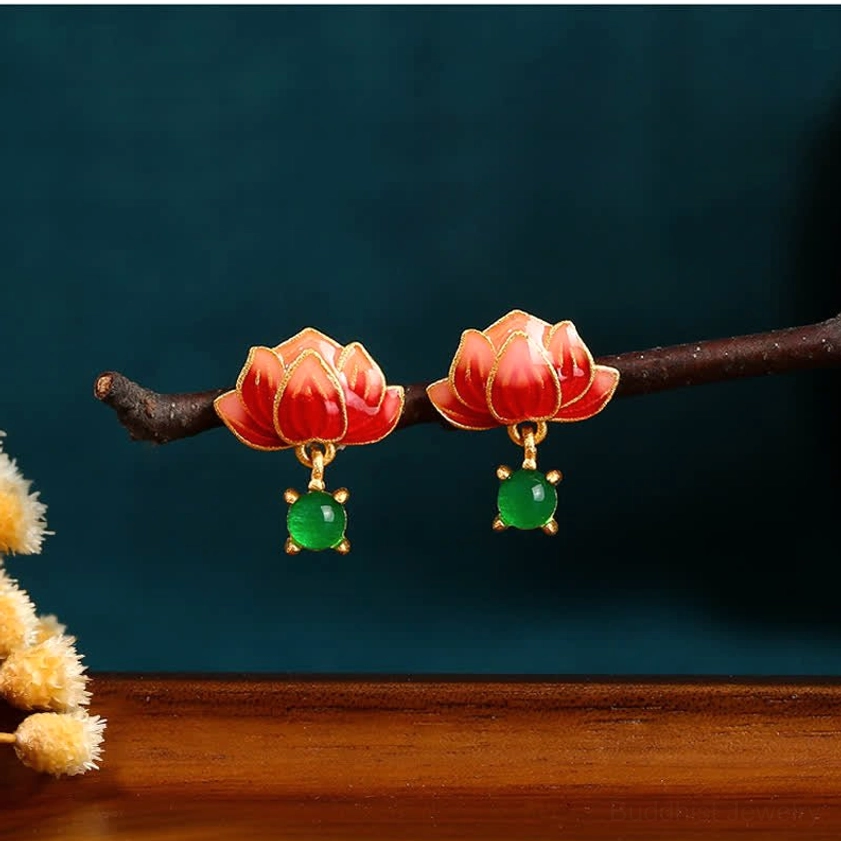 Flat lay of lotus enamel dangle earrings on wooden branch with dried flowers, featuring red lotus design and caged green jade drop pendant