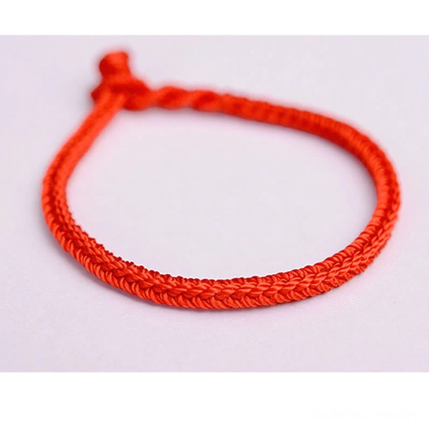 Front view of solid red Buddhist peace knot string bracelet with braided cord and tied knot on white background
