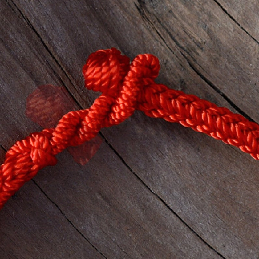 Close-up detail of red braided Buddhist peace knot bracelet showing woven cord texture and tied decorative knot