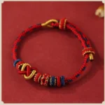 Red and gold peace knot Buddhist bracelet flat lay - handcrafted adjustable string design with protective spiritual symbolism
