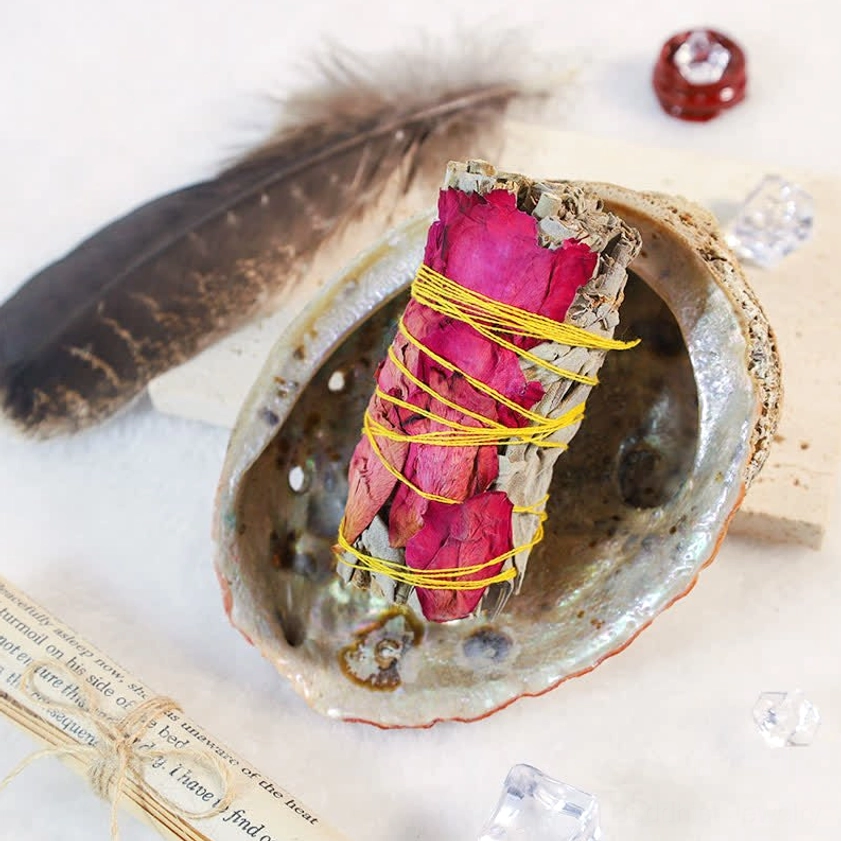 Red rose petal smudge stick wrapped with yellow twine resting in abalone shell on sacred display