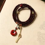 Red rosewood 108 bead mala with peace buckle pendant displayed flat lay on vintage patterned paper, showing deep reddish-brown beads and red peace buckle accent