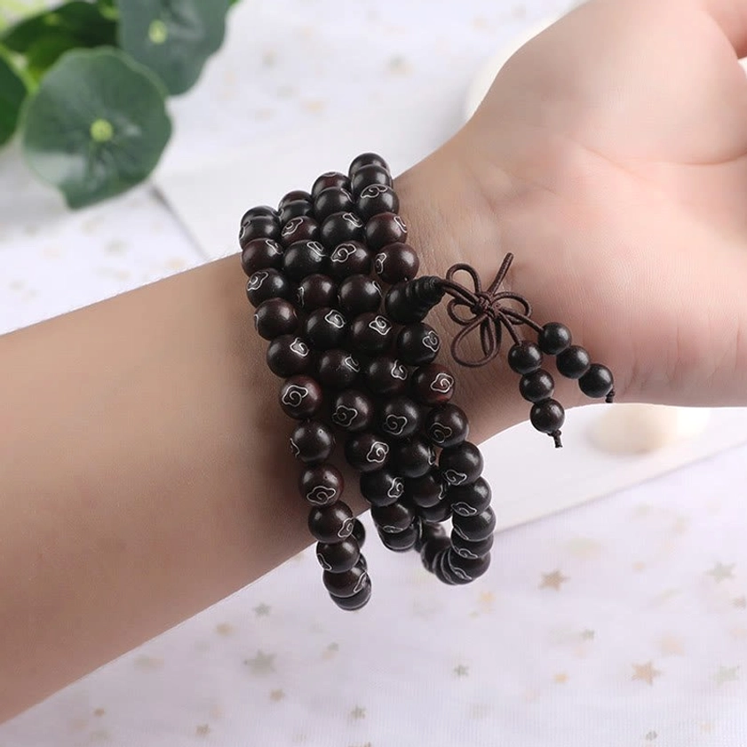 Adjustable multi-loop red sandalwood bracelet with tassel knot worn on wrist against star-patterned background