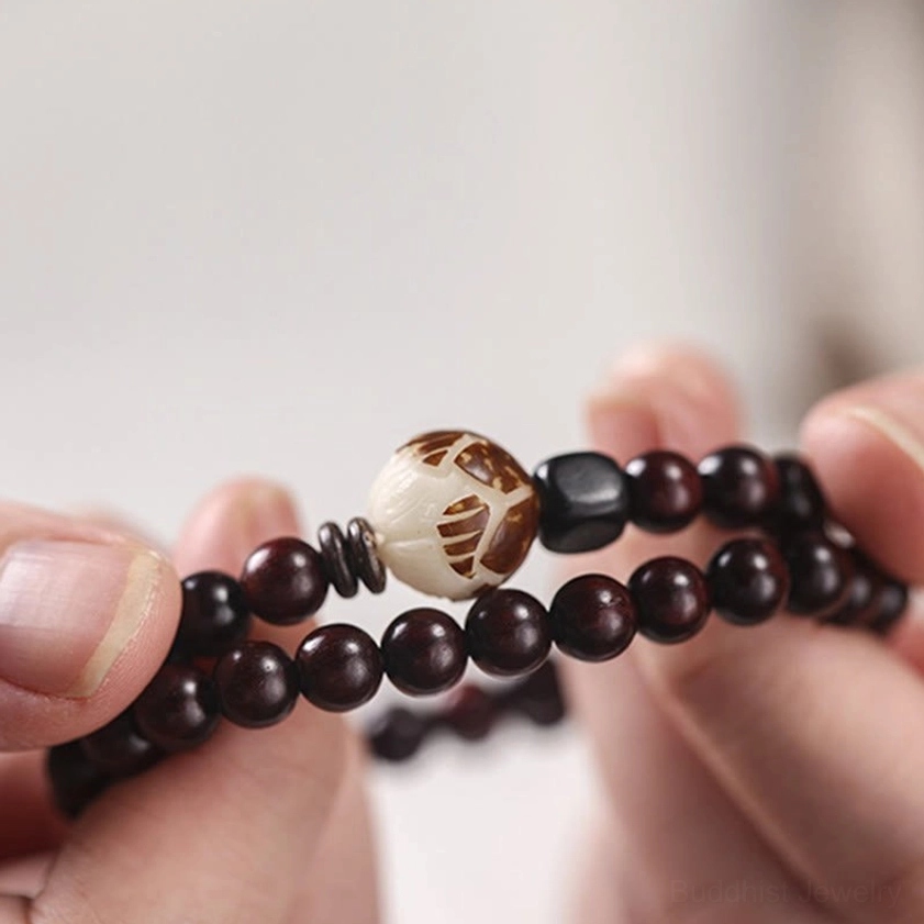 Close-up handheld view of red sandalwood bracelet showing individual dark red wooden beads, carved lotus bead focal point, and black spacer accents