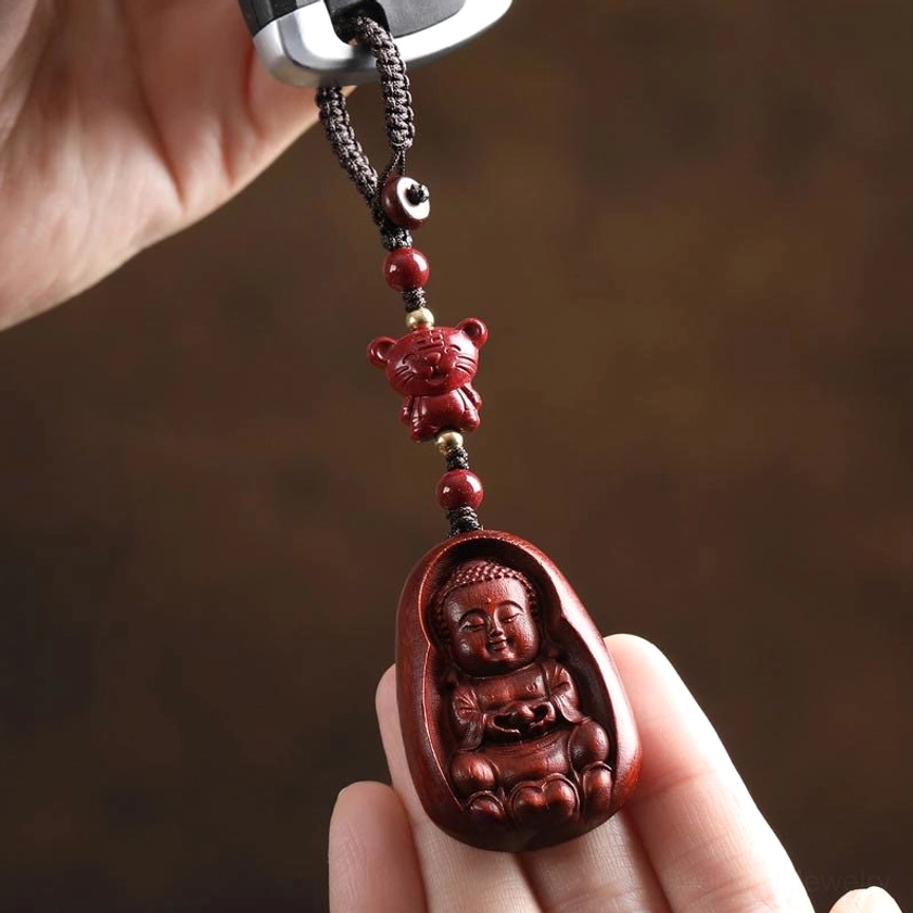 Red sandalwood zodiac Buddha keychain held with car key showing baby Buddha relief carving and hand detail