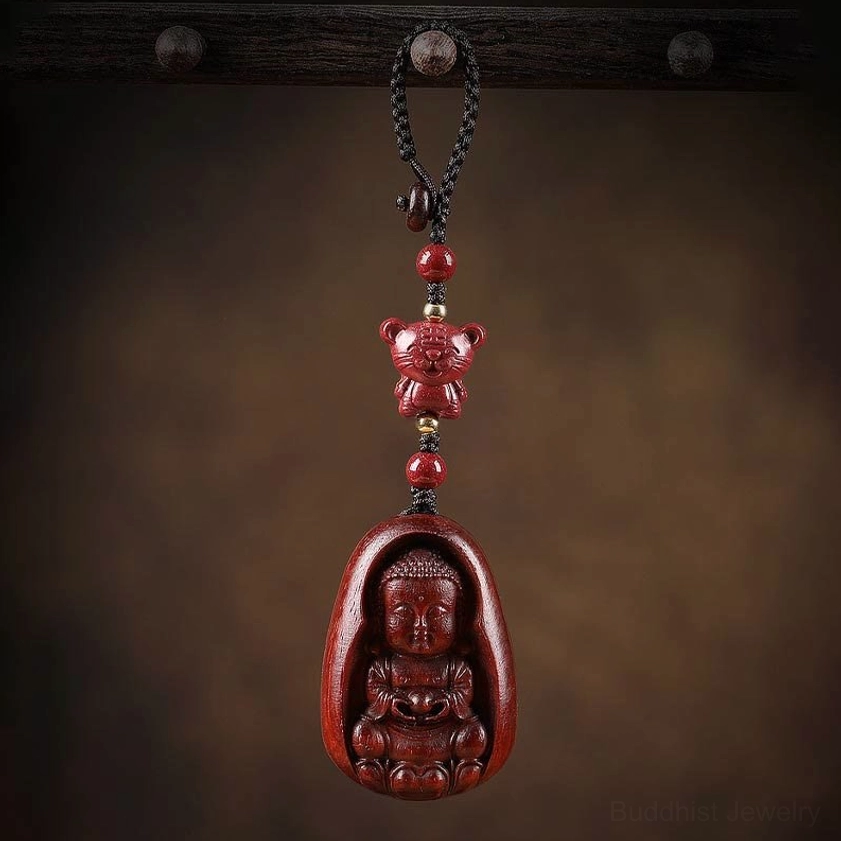 Red sandalwood zodiac Buddha keychain overhead view on wooden hook backdrop with braided black cord detail
