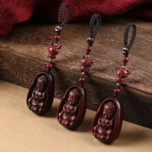 Red sandalwood Buddha zodiac keychains flat lay with black braided cord and red cinnabar beads on wooden table with fabric backdrop