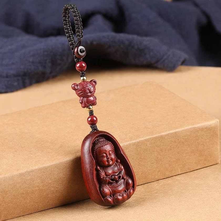 Red sandalwood zodiac Buddha keychain side lay view showing red animal bead and smooth wood texture on cloth backdrop