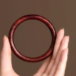 Red Sandalwood Buddhist Protection Bracelet held in palm - front close-up view showing reddish-brown polished wood grain