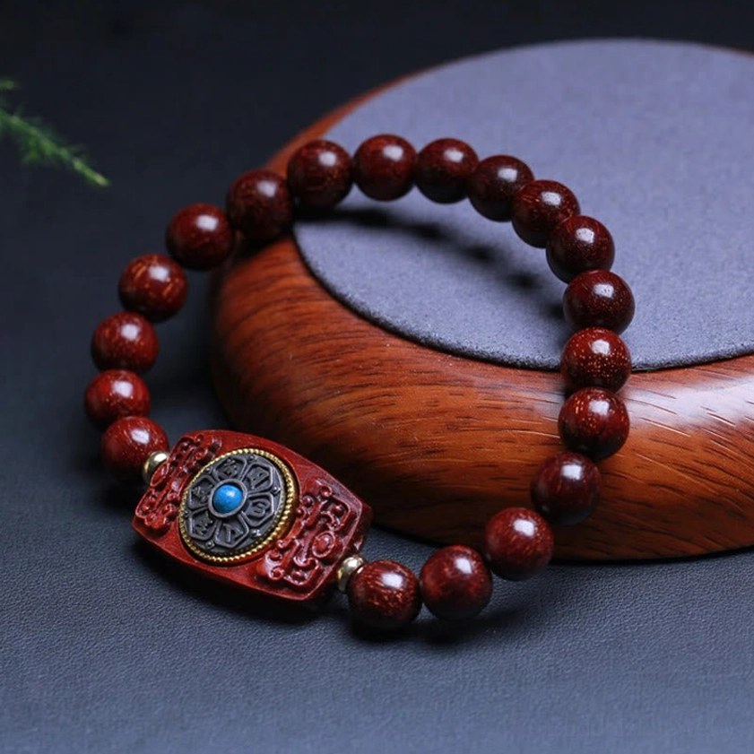 Dark red sandalwood Buddhist bracelet with decorative charm featuring blue gemstone inlay, three-quarter display view