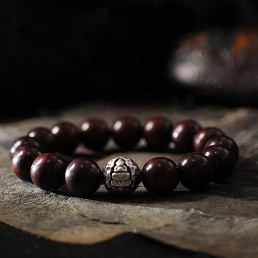 Red sandalwood Buddhist bracelet with 999 sterling silver Buddha charm, angled close-up showing deep burgundy wood beads and protective spiritual energy