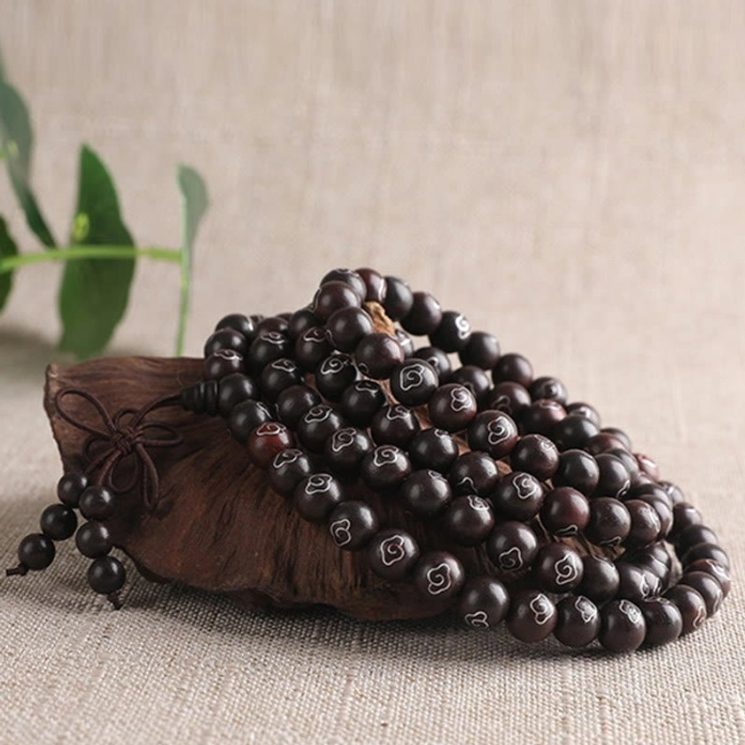 Coiled red sandalwood Buddhist bracelet with sterling silver motifs and fabric tassel knot on linen background