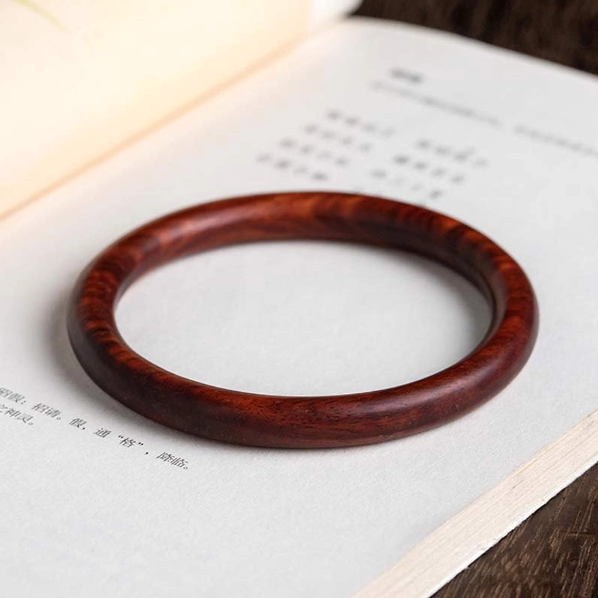 Red Sandalwood Buddhist bangle on vintage paper - top-down view showing natural wood grain detail
