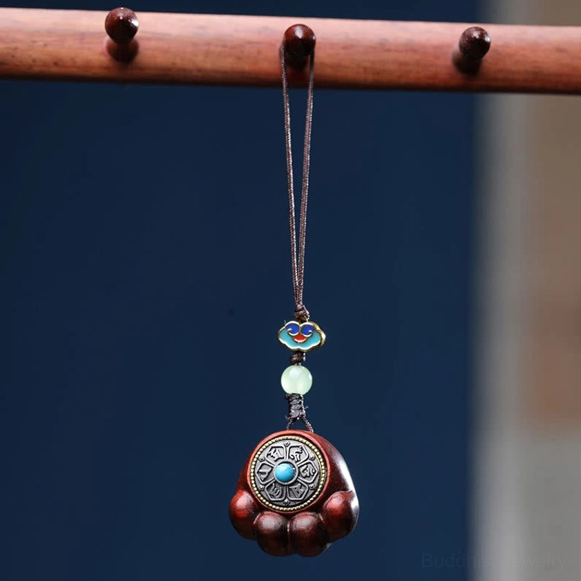 Close-up of red sandalwood cat paw phone charm with enamel cloud decoration, jade bead, and turquoise-inlaid metal charm accent