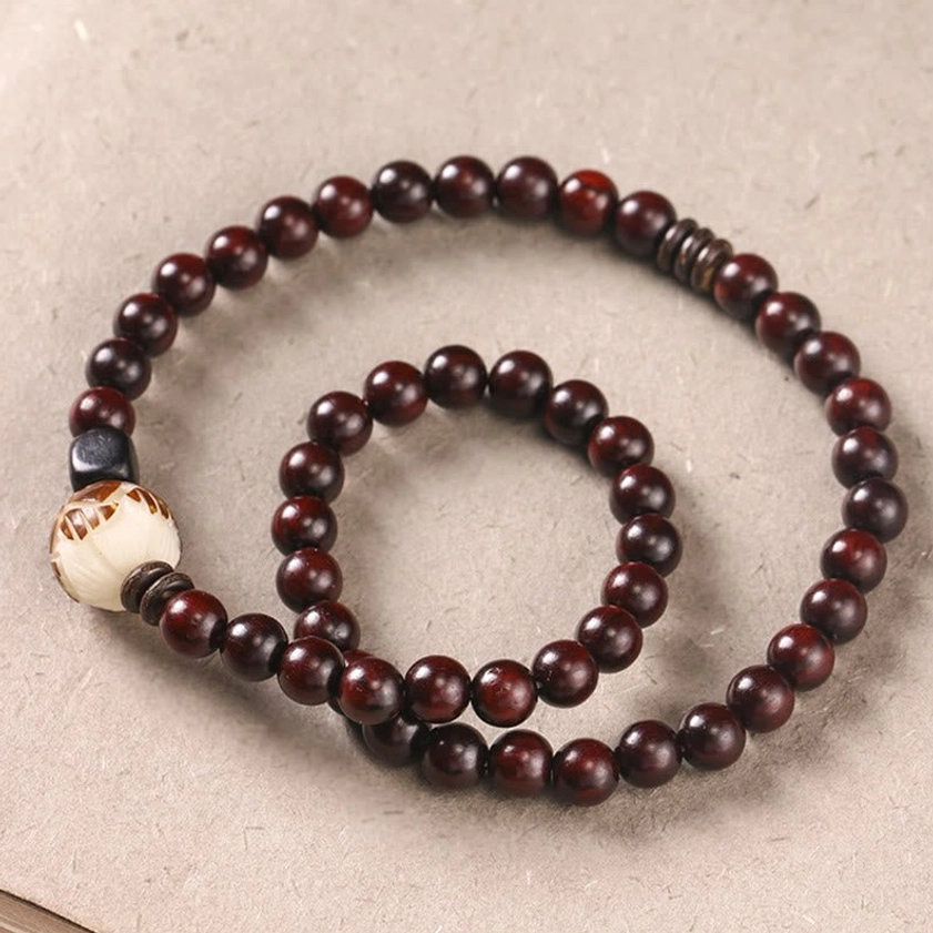 Top-down flat lay of red sandalwood double wrap bracelet on light fabric, displaying glossy deep red wooden beads and two-strand layered design