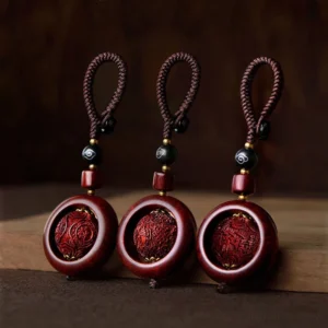 Set of three red sandalwood and ebony rotating prayer keychain pendants with carved Buddhist mantras displayed on wooden surface