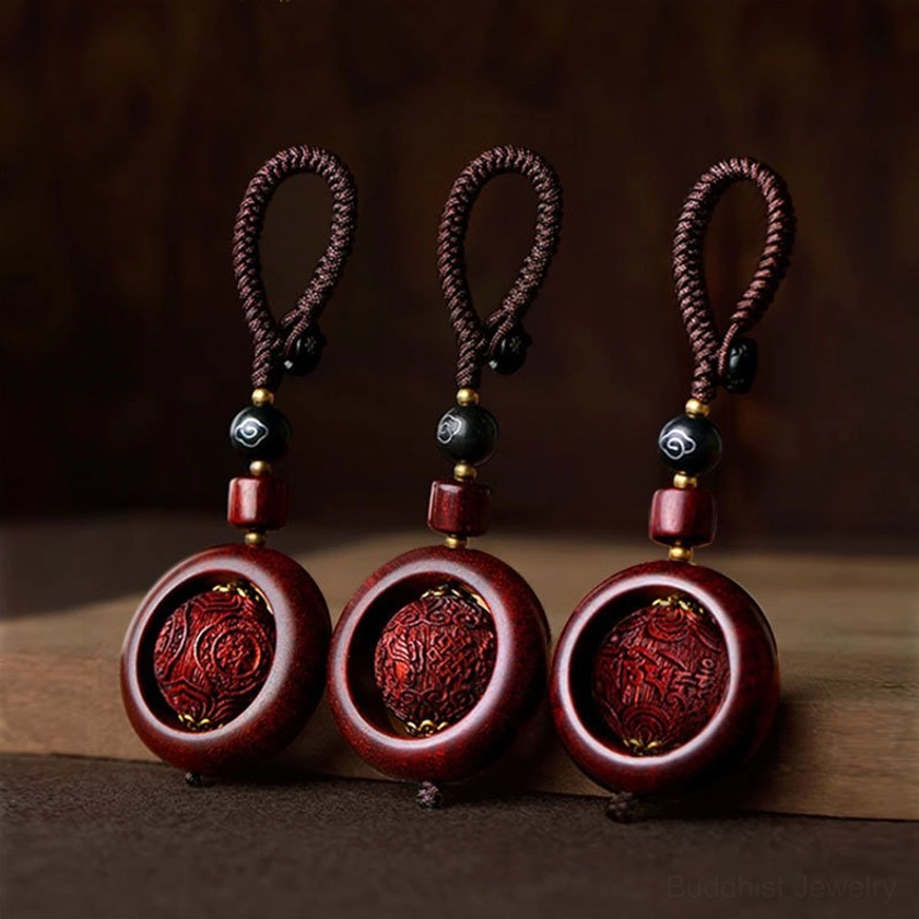 Set of three red sandalwood and ebony rotating prayer keychain pendants with carved Buddhist mantras displayed on wooden surface