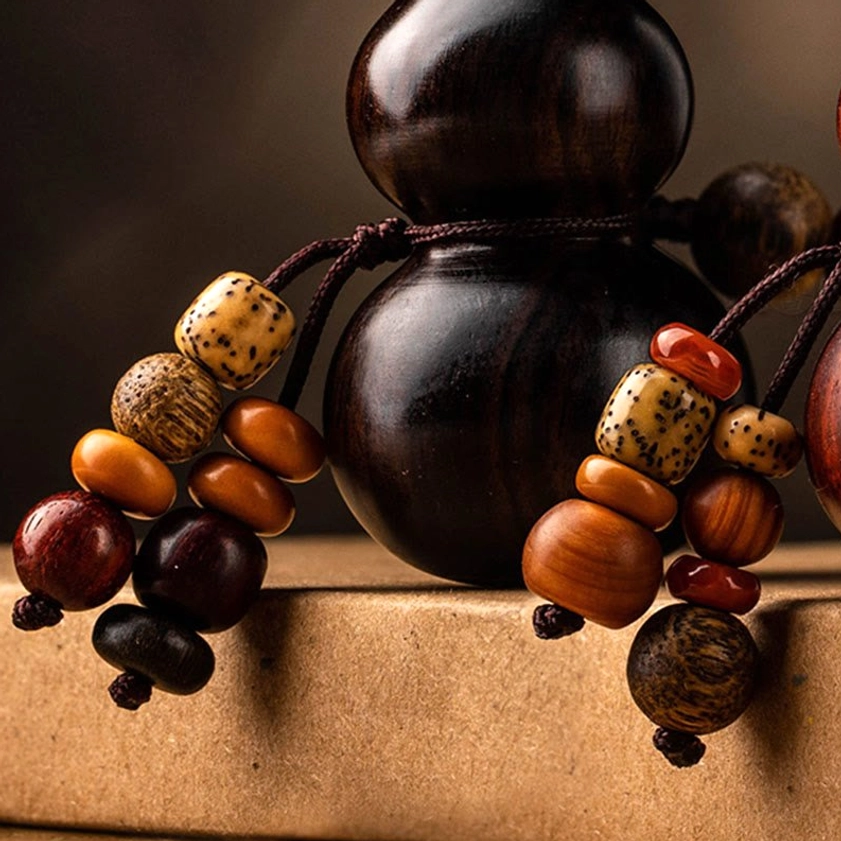 Overhead close-up of red sandalwood gourd keychain on wooden surface, revealing fine grain texture and traditional Buddhist hand-carved details