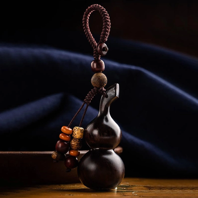 Sacred red sandalwood gourd keychain side view on dark blue fabric, showing natural wood grain texture and braided rope hanging strap for inner peace