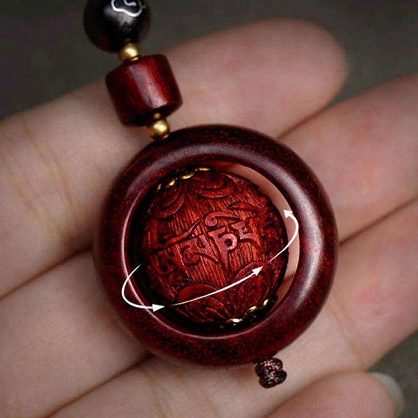Extreme close-up of red sandalwood rotating prayer keychain in human palm displaying visible wood grain and rotatable carved sphere