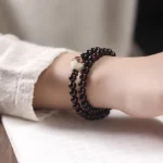 Red sandalwood lotus bodhi double wrap bracelet worn on wrist, showing deep red carved wooden beads with lotus focal bead and black spacer details