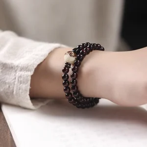 Red sandalwood lotus bodhi double wrap bracelet worn on wrist, showing deep red carved wooden beads with lotus focal bead and black spacer details