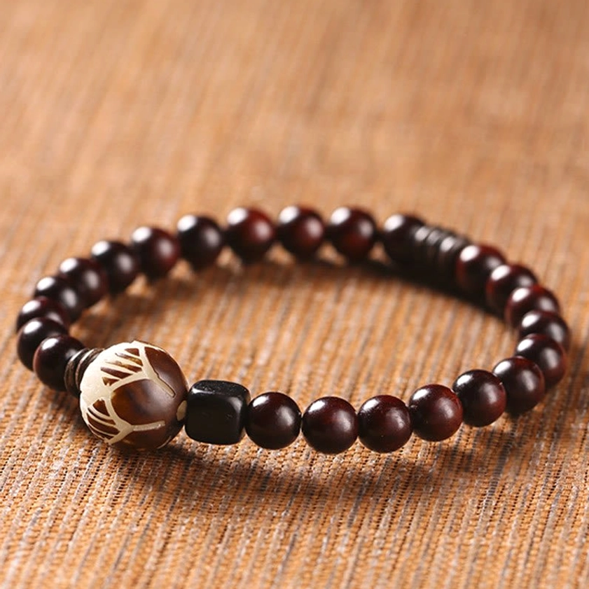 Single wrap wooden bracelet with glossy dark red sandalwood beads on woven brown fabric, featuring hand-carved lotus accent and black square spacers