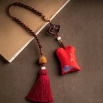 Red sandalwood lotus car hanging sachet with embroidered peace blessing, blue cloud pattern, wooden charm, and red tassel on tabletop