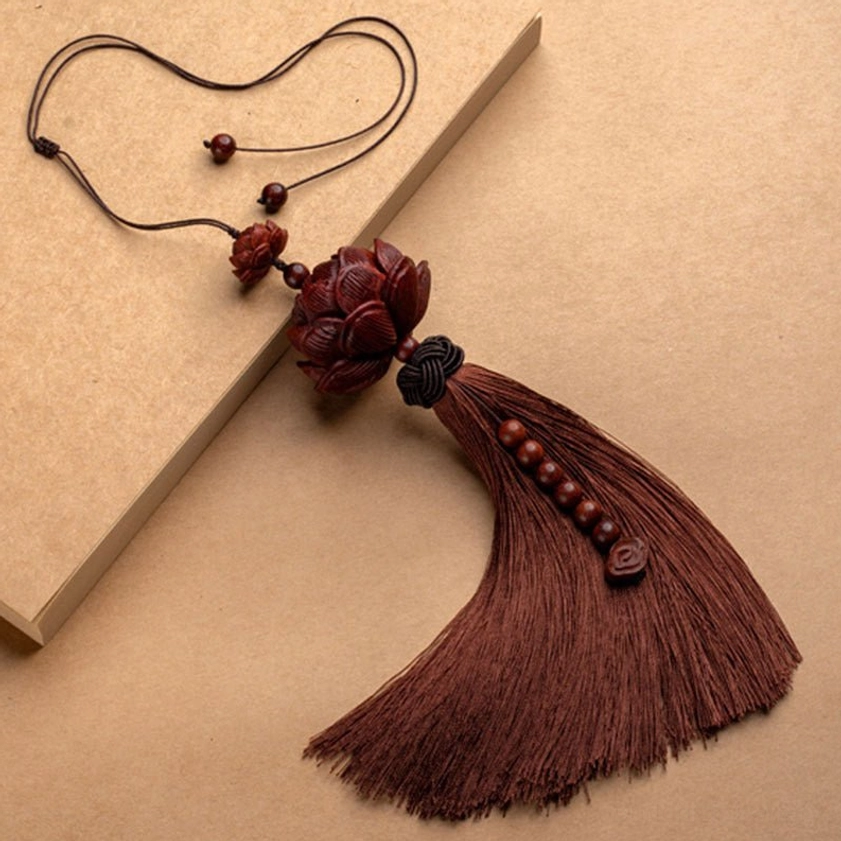 Single handmade red sandalwood lotus tassel with dark braided knot and wooden beads on kraft paper background