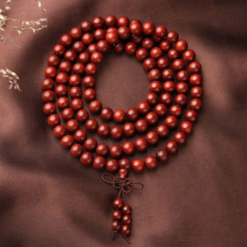 Top view of 108 bead red sandalwood mala circular arrangement with tassel pendant and natural wood decor