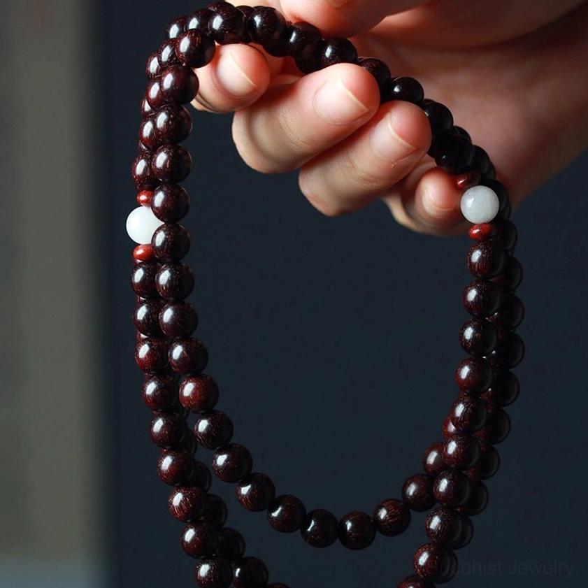Side view of sandalwood prayer mala being held showing reddish-brown polished beads with white spacer beads and carved pendant