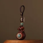 Red sandalwood money bag Buddhist charm with turquoise-inlaid rotatable front, braided cord attachment, and ping an peace bead - front view