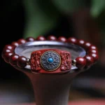Small leaf red sandalwood Buddhist bracelet with carved Om Mani Padme Hum charm and turquoise inlay, displayed on dark ceramic holder