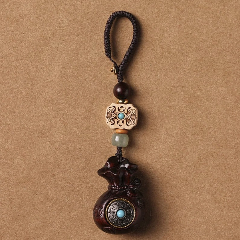 Small leaf red sandalwood Om Mani Padme Hum keychain with braided black rope and turquoise stone accent on kraft paper