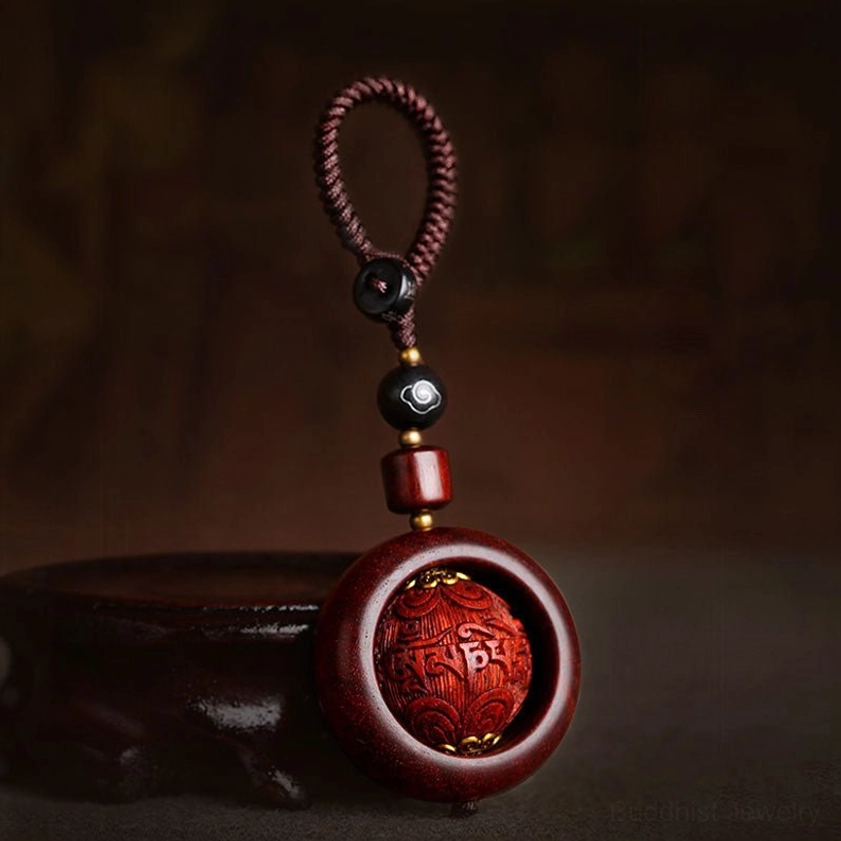 Close-up side view of red sandalwood rotating prayer bead keychain with carved mantra sphere and black ebony accent beads