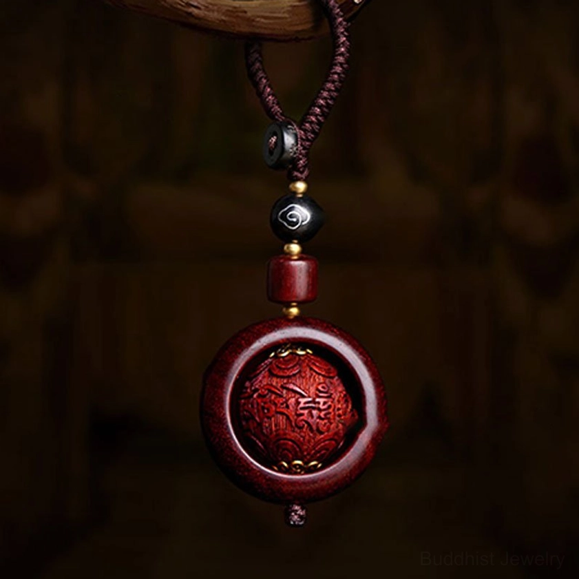 Close-up front view of red sandalwood rotating prayer keychain with carved Buddhist mantra design on dark vintage background