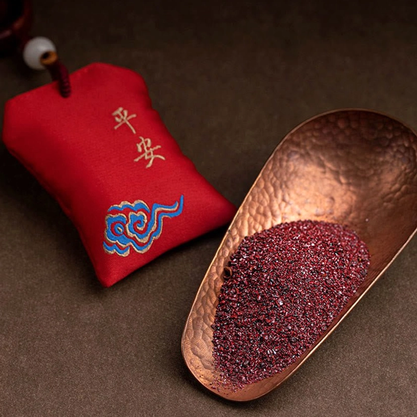 Red sandalwood sachet with peace embroidery and cinnabar powder sample shown with traditional copper scoop on tabletop still life