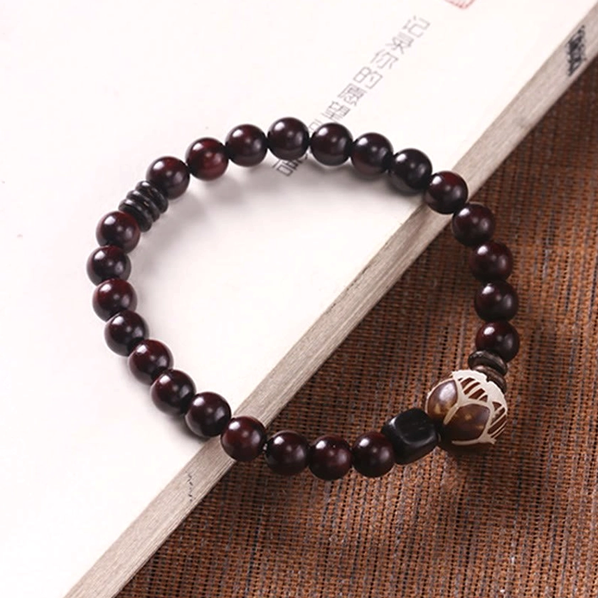 Single wrap red sandalwood bracelet with carved lotus focal bead on book and brown fabric background, showing unisex design and protection bracelet styling