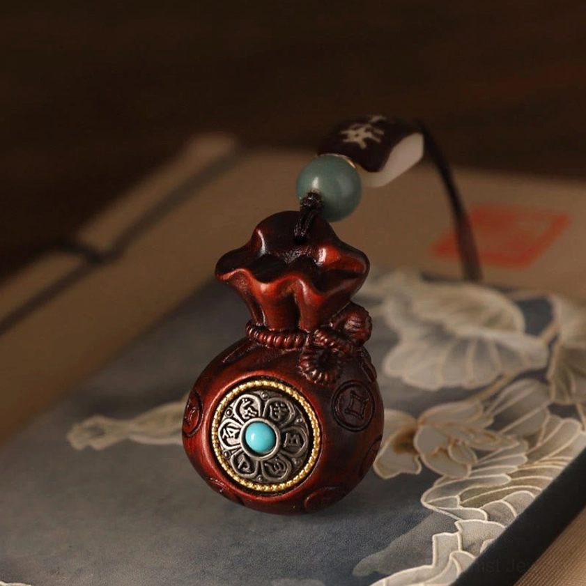 Red sandalwood Buddhist money bag charm with stitched money bag texture and turquoise-inlaid charm on decorative fabric background